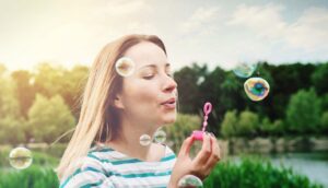 Woman blowing bubbles with trees behind her